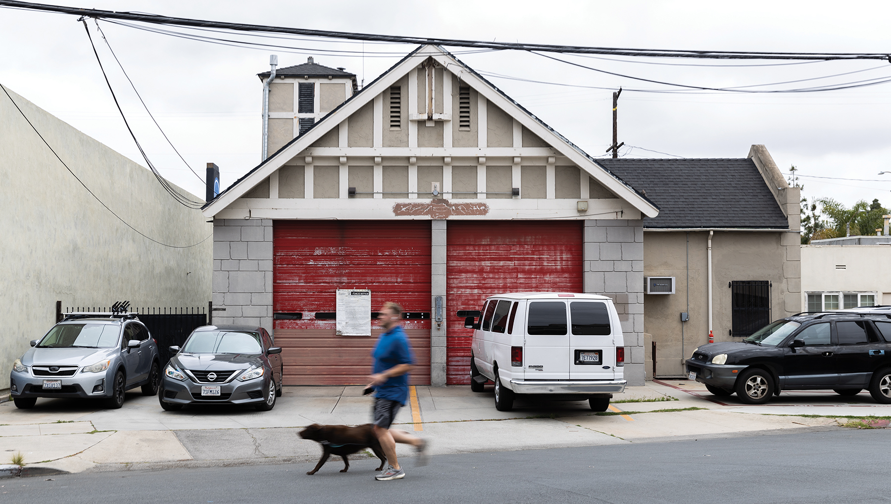 A man in a blue shirt runs past a dilapidated firehouse with his black dog.