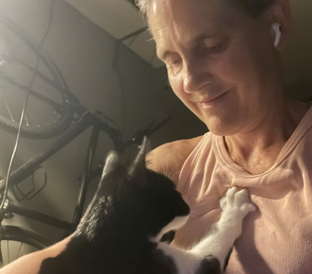 Woman with gray hair looking lovingly at black-and-white cat, who has paw on her chest