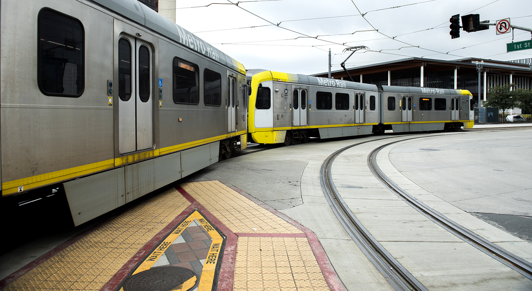 A light rail train that says "Metro Rail" curves on a track underneath a traffic light.