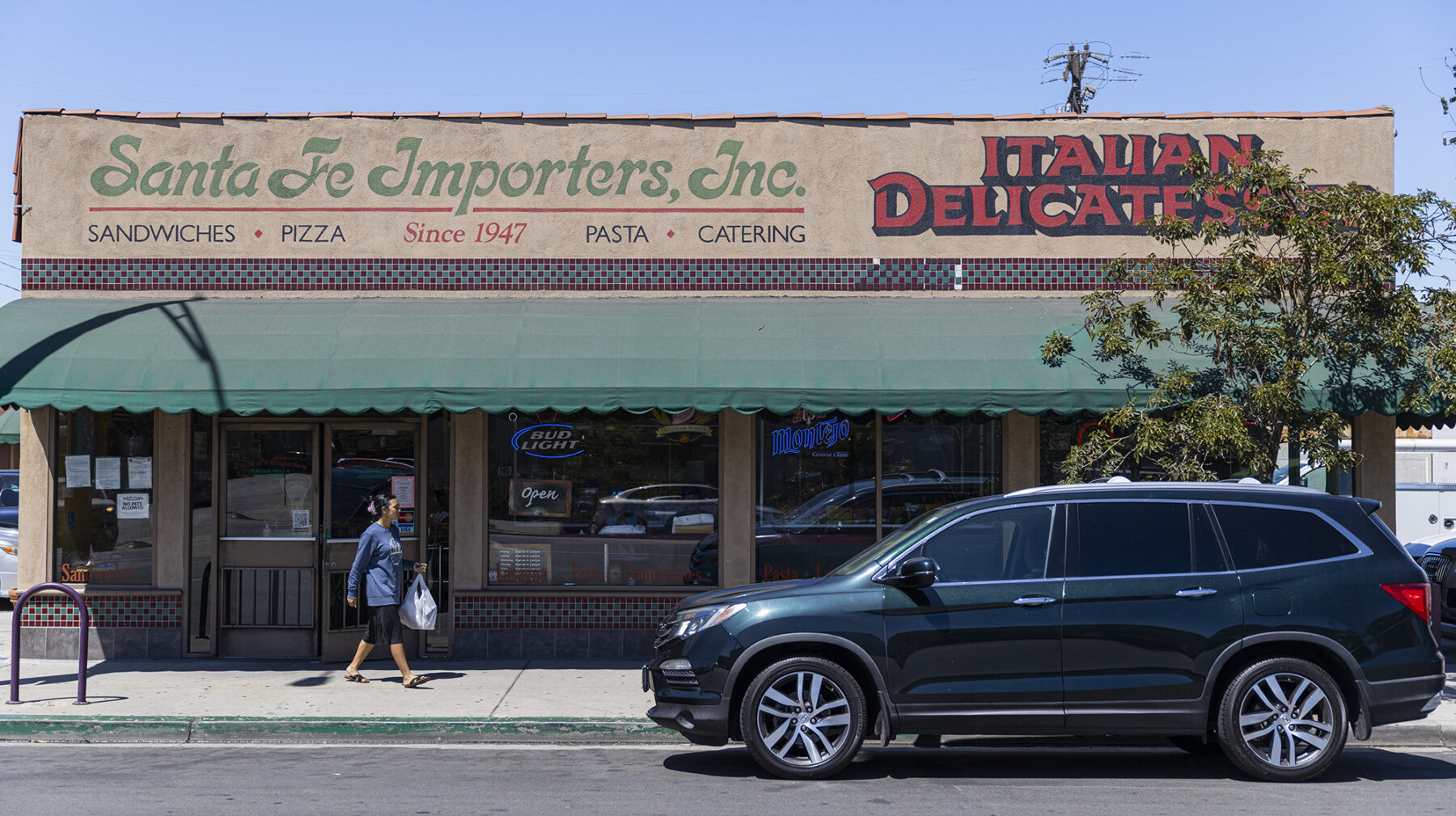 An SUV is parked in front of a one-story building that says "Santa Fe Importers, Inc. Italian Delicatessen."