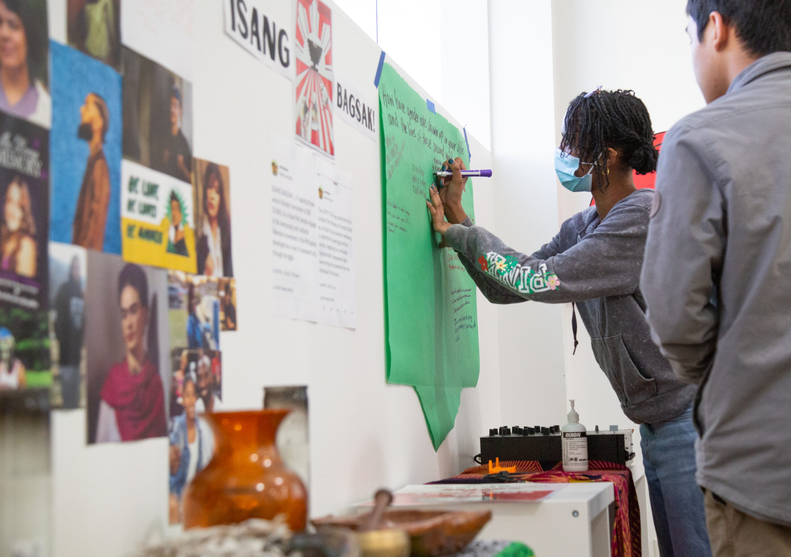 A student writes on a green poster that is hung on a wall.
