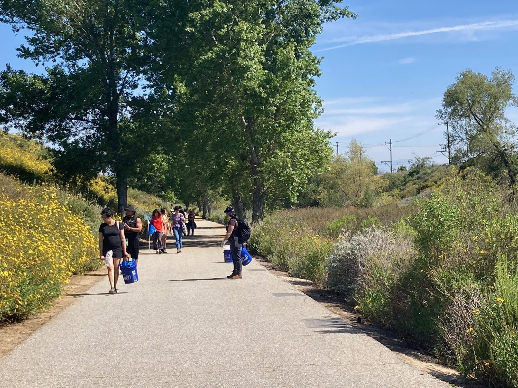 A group people with clean-up supplies walks along a path at the Dominguez Gap Wetlands.