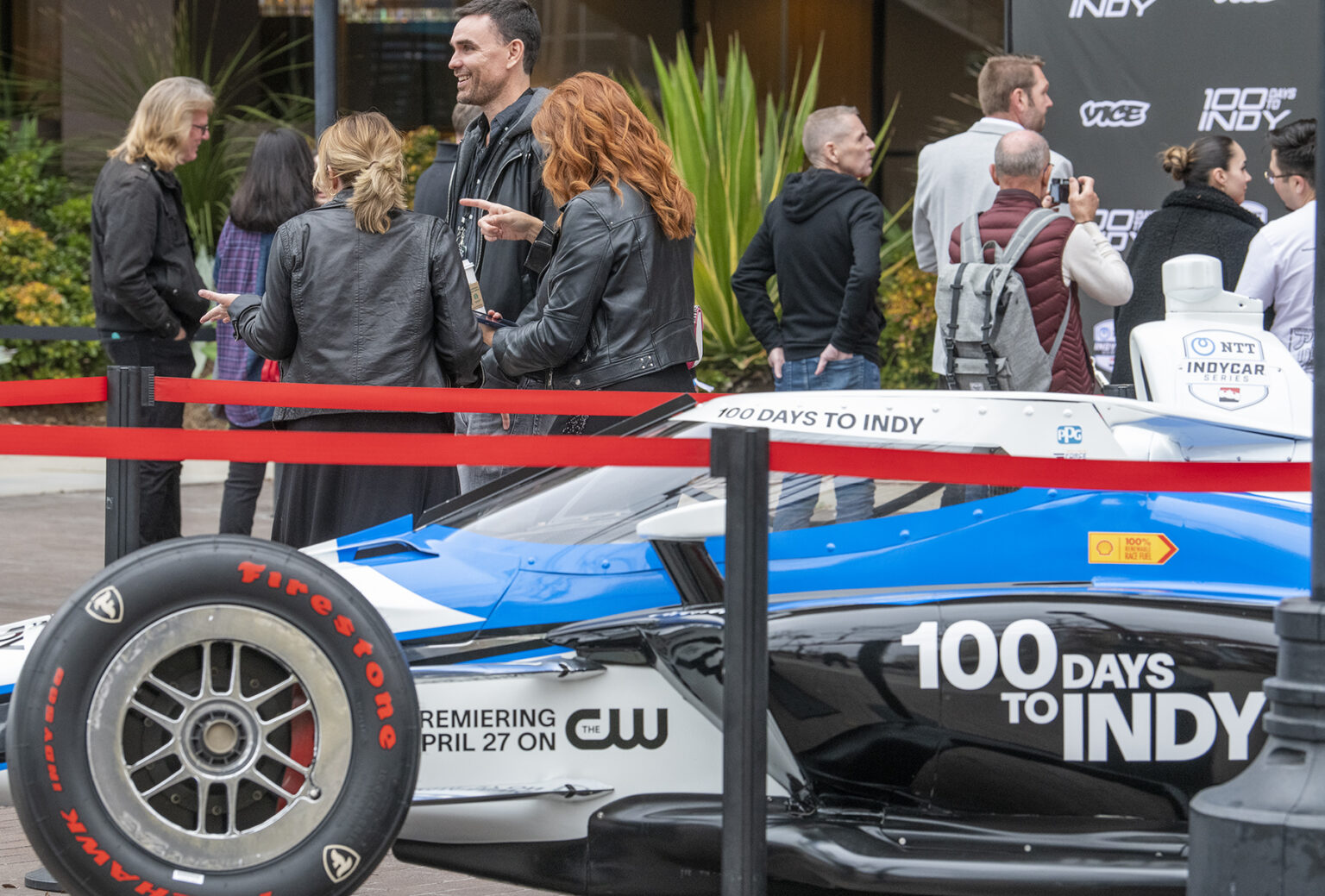 A racecar that says "100 Days to Indy" sits behind red carpet tape.