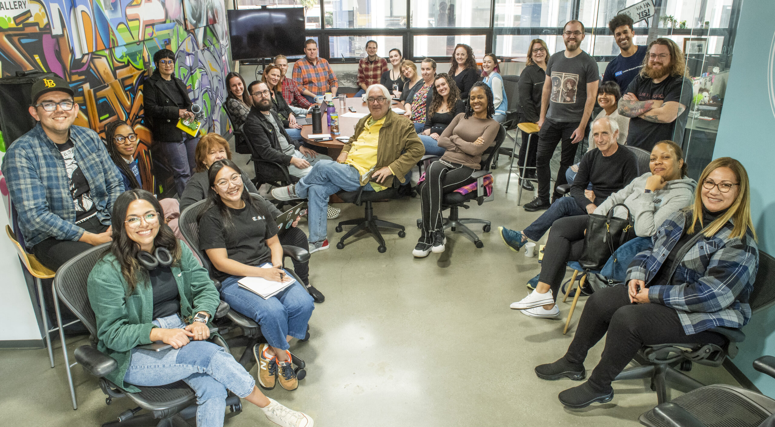 A large group of people sit in an office and smile for the camera.