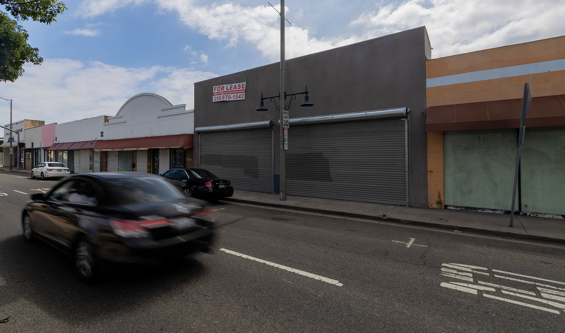 A black car drives by vacant storefronts.