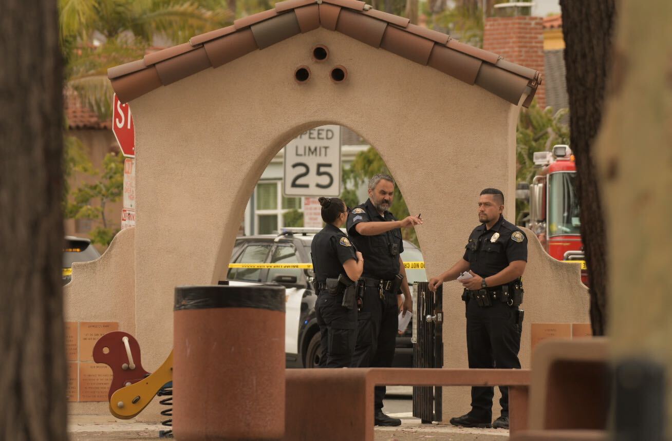 Three police officers stand behind a bench and trash can in a park.