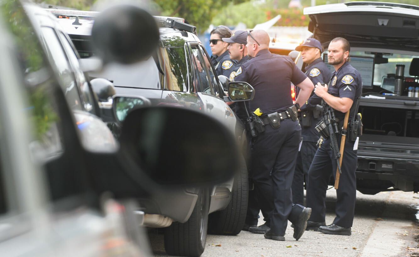 Police officers huddle around a police SUV.