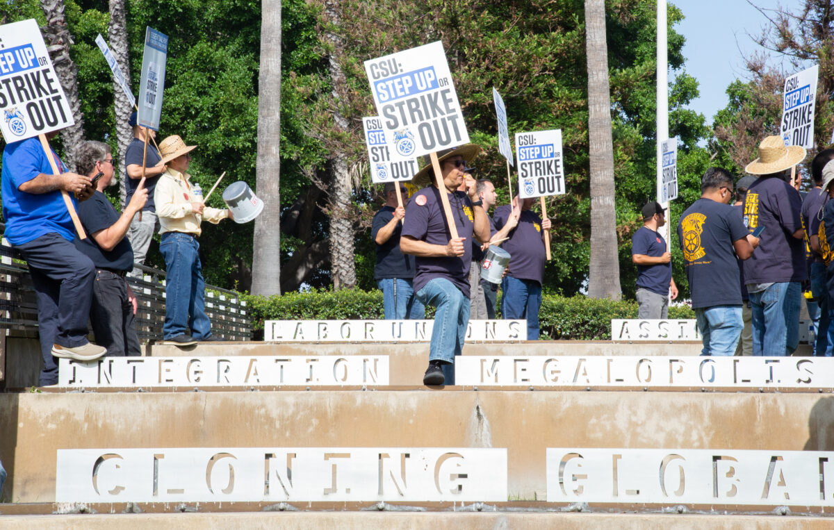 Union member protesters with signs reading "CSU: Step Out or Strike Out," whistle over steps that say words varying from "Labor Unions," "Integration," and "Cloning Global."