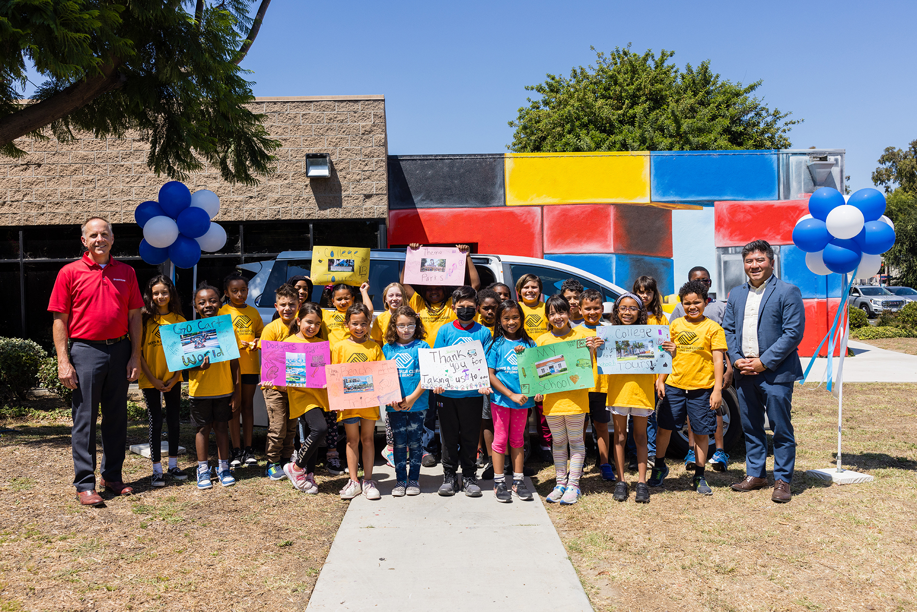 A group of kids stand in front of a van, holding posters that say "thank you."