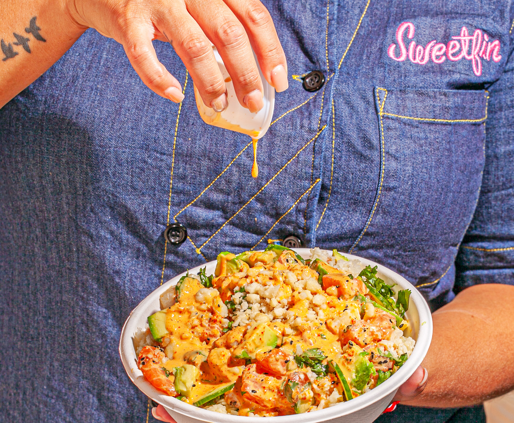 A woman pours aioli sauce onto a Sweetfin poke bowl.